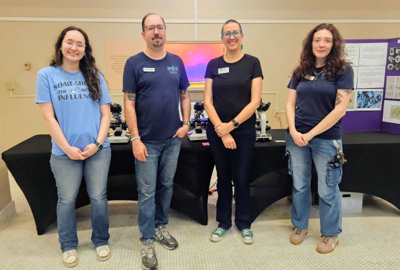 Four people standing in front of tables.